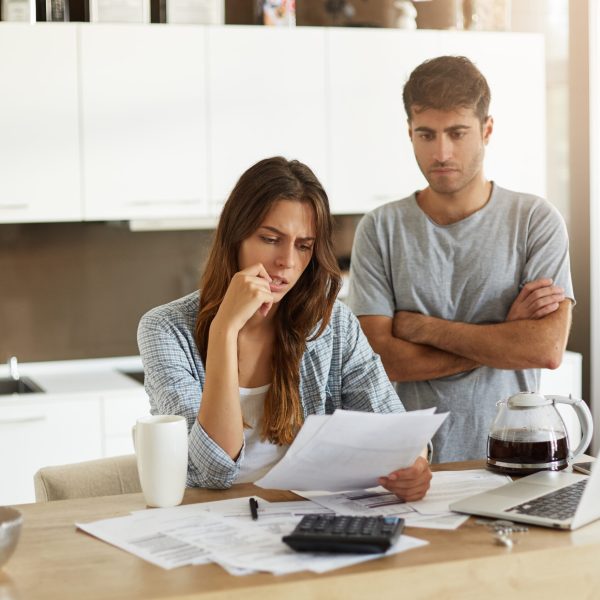 Candid shot of young American man and woman dressed casually feeling stressed while managing finances in kitchen together, calculating expenses, paying utility bills online on laptop computer