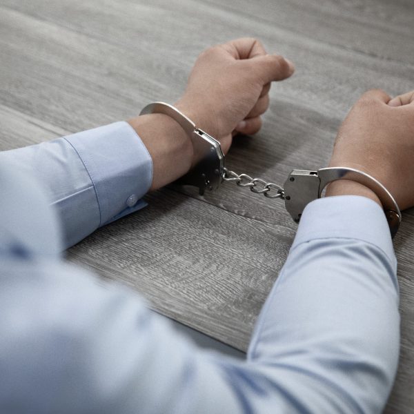 A selective focus shot of male hands in handcuffs on a wooden table