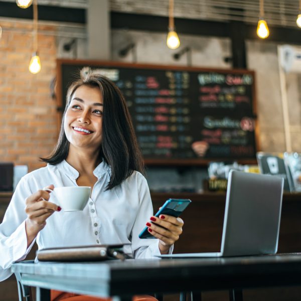 woman sitting happily working with a smartphone in a coffee shop and notebook.